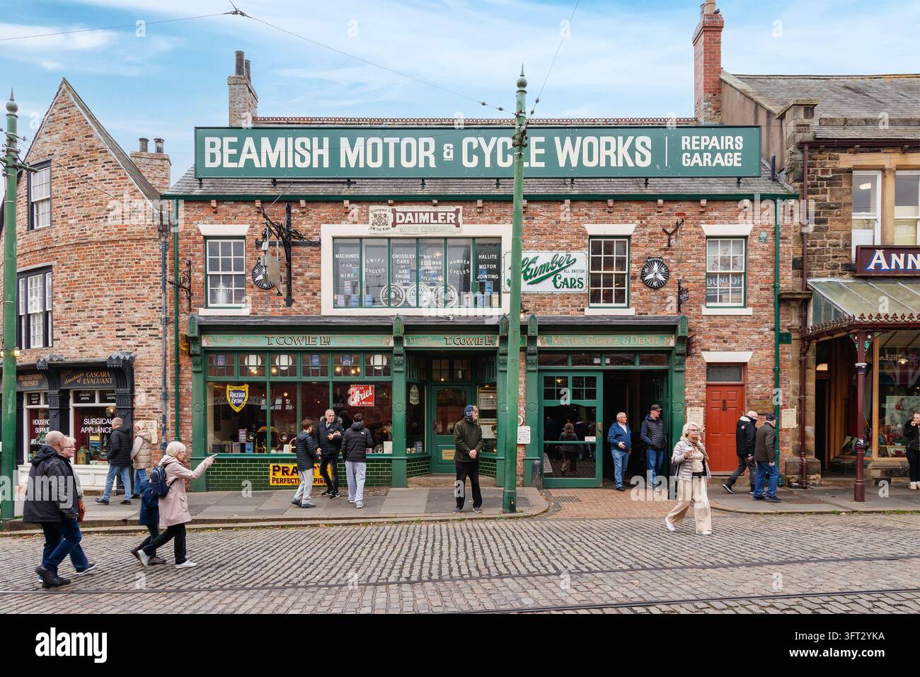 Beamish Motor and Cycle Works al Beamish Museum, una vetrina del negozio in mattoni rossi con finiture verdi e visitatori sulla strada Foto Stock