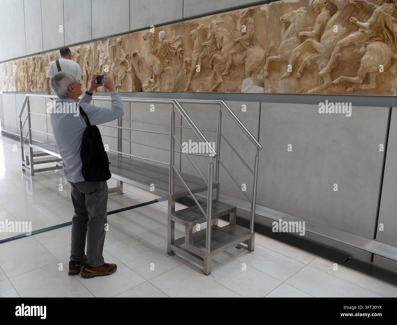 ATENE, GRECIA - 16 MAGGIO 2025 - Partenone - Viaggiatore maturo che fotografa antichi manufatti in marmo del Partenone nel sito storico di Atene Foto Stock