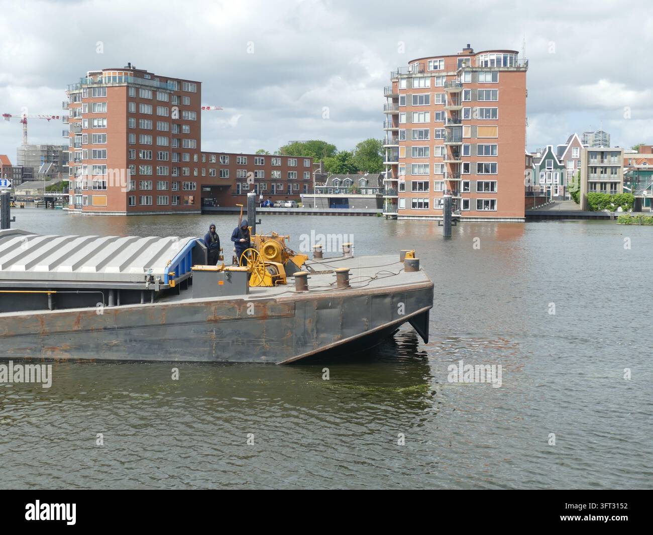 AMSTERDAM - 23 MAGGIO 2025 - Chiatte industriale con operai e macchinari che navigano nei canali di Amsterdam, Paesi Bassi, mostrando lo sviluppo urbano Foto Stock