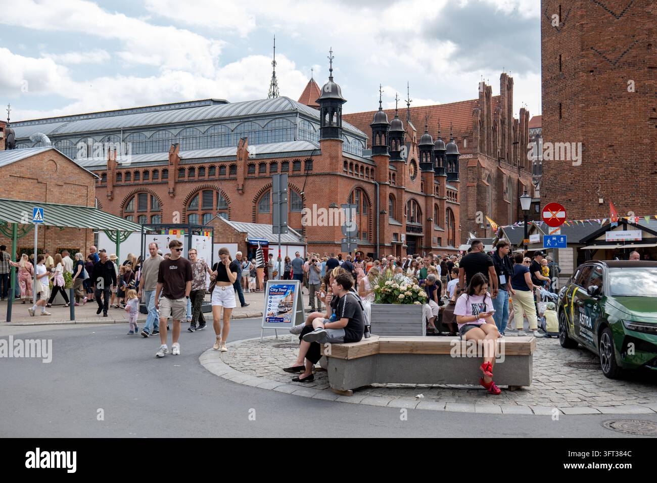 Giornata estiva sulla piazza acciottolata davanti alla sala del mercato Hala Targowa a Danzica, Polonia. Folle di turisti e locali passano davanti alle bancarelle del mercato Foto Stock