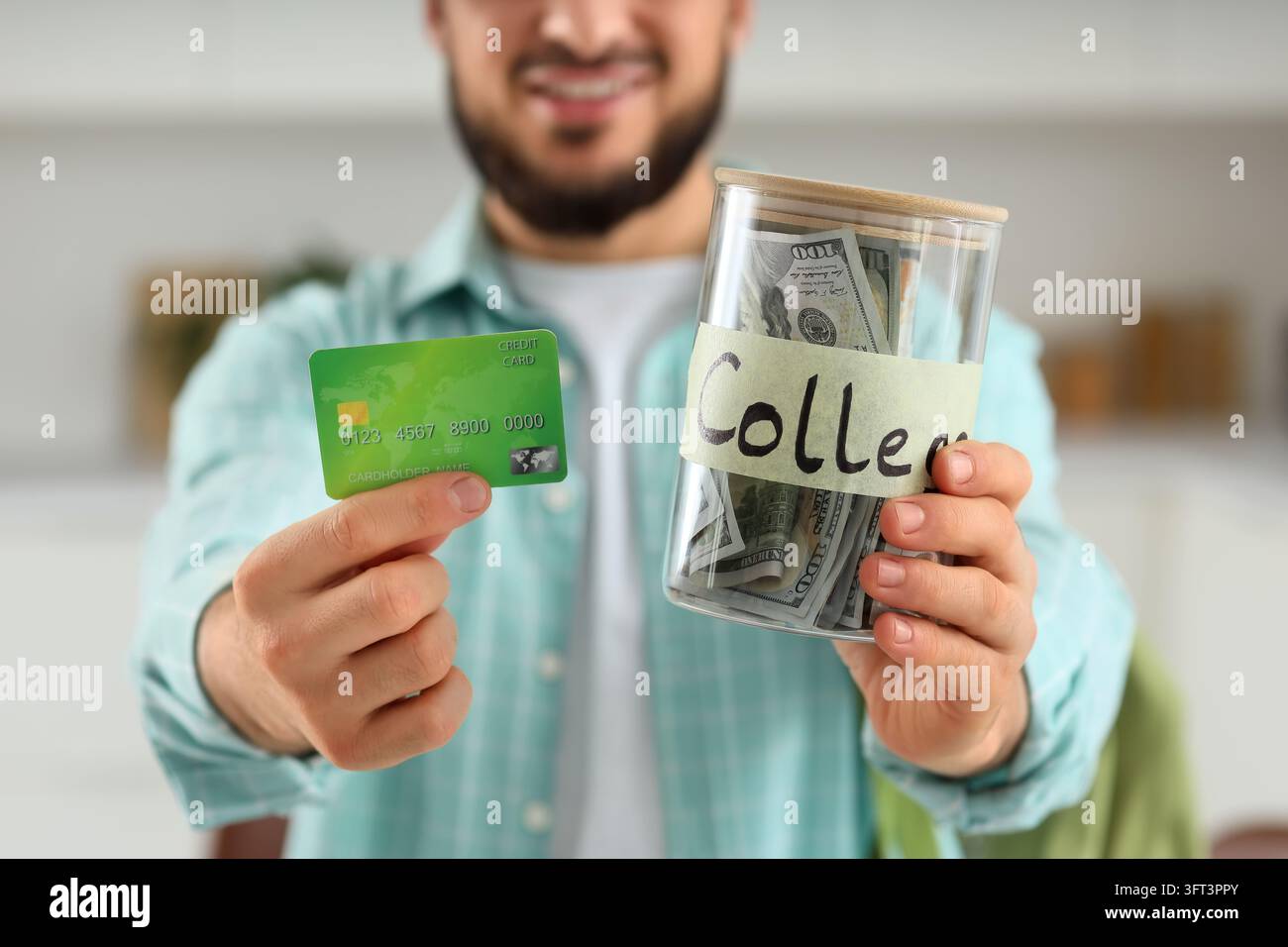 Risparmi per il college e debiti di istruzione, uomo che tiene una carta di credito e un barattolo di vetro con denaro contante per le tasse universitarie e la pianificazione dei prestiti studenteschi in una cucina domestica Foto Stock