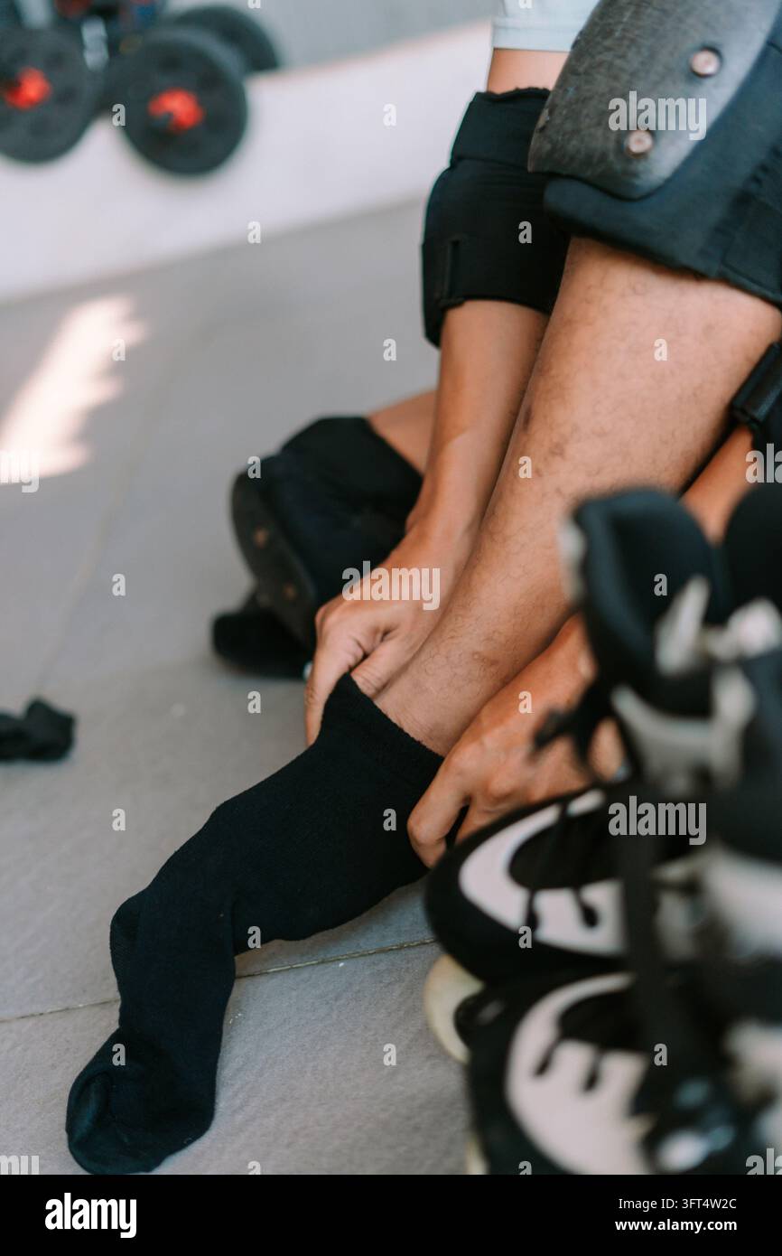 Prima di una persona che indossa calzini neri prima di pattinare con i pattini a rotelle, con ginocchiere protettive su un terreno pavimentato all'aperto. Foto Stock