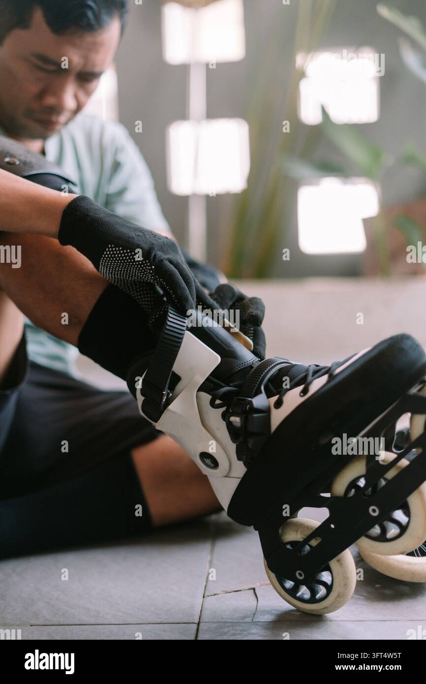 Una persona adulta seduta al chiuso mentre allaccia e regola le fibbie di pattini a rotelle neri e bianchi per il tempo libero all'aperto e uno stile di vita attivo. Foto Stock