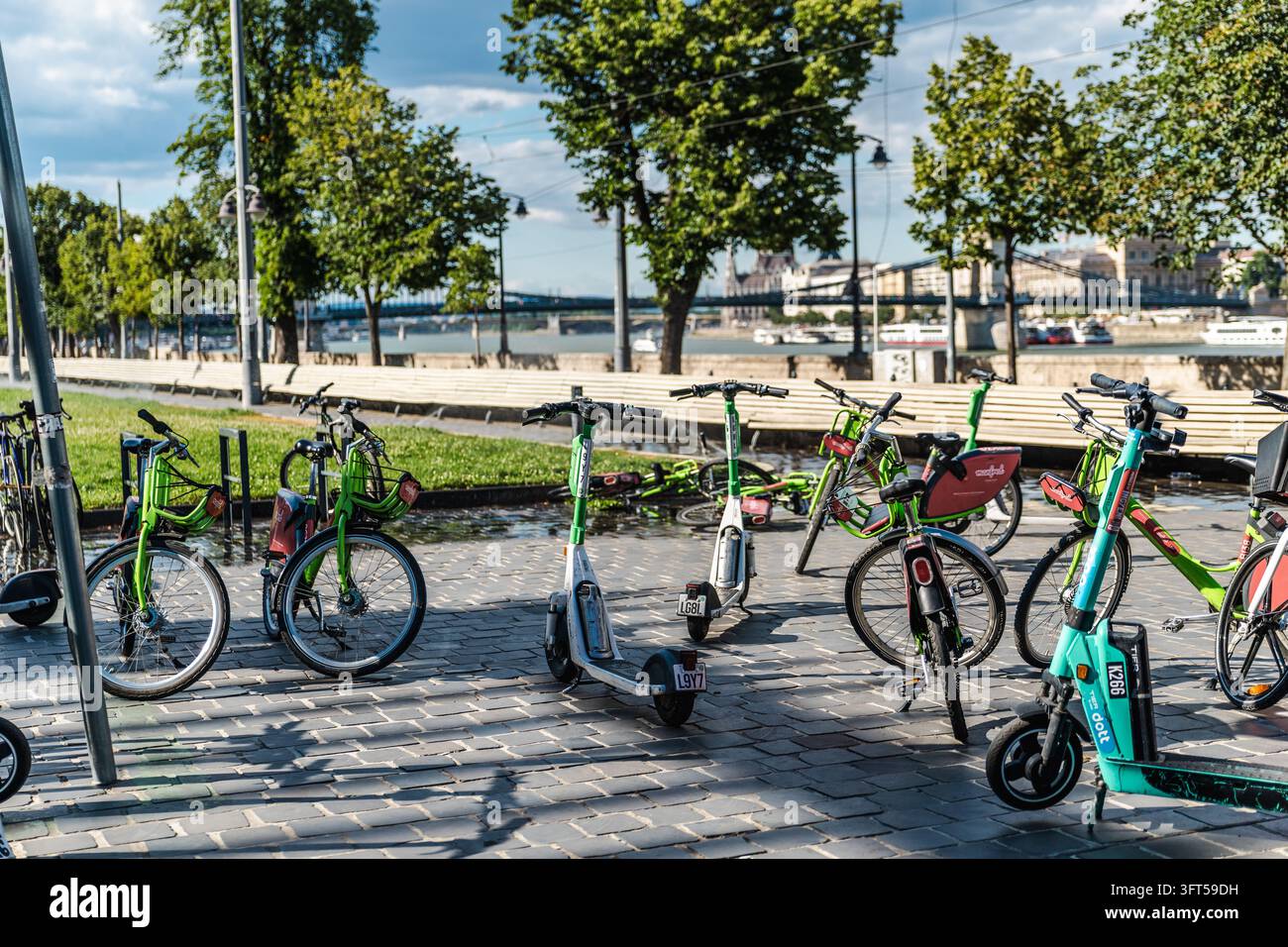 Budapest, Ungheria, 25 giugno 2026: biciclette a noleggio e scooter elettrici costeggiano una passeggiata sul lungofiume accanto al Danubio. Foto Stock