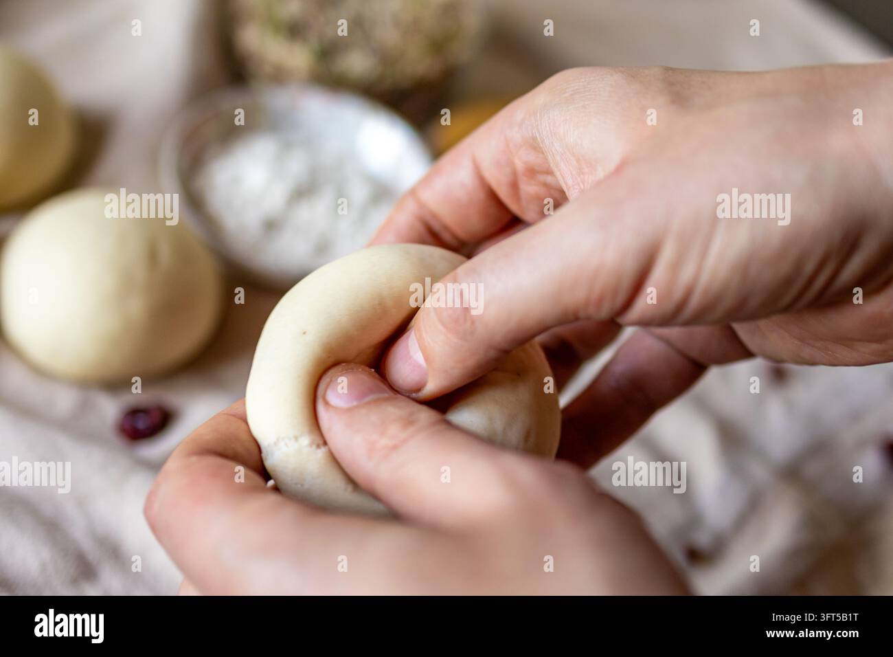 Le mani modellano una morbida palla di impasto in un anello per bagel fatti in casa su un asciugamano di lino in una cucina luminosa. Concetto di panificazione artigianale e del professionista creativo Foto Stock
