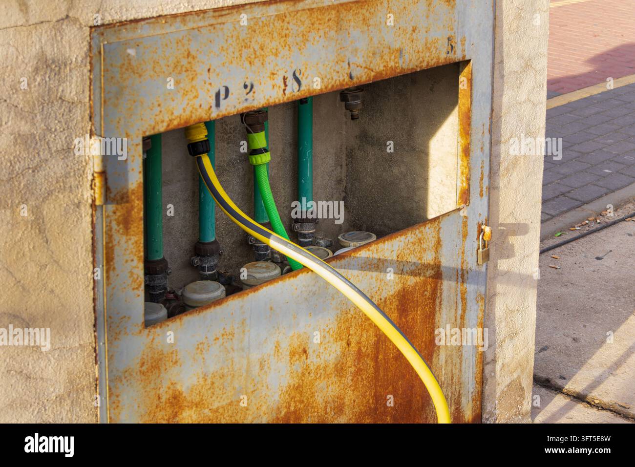 Armadio per l'approvvigionamento idrico arrugginito con tubo da giardino collegato e contatori idraulici, che evidenzia le infrastrutture comunali e i sistemi di distribuzione dell'acqua. Foto Stock