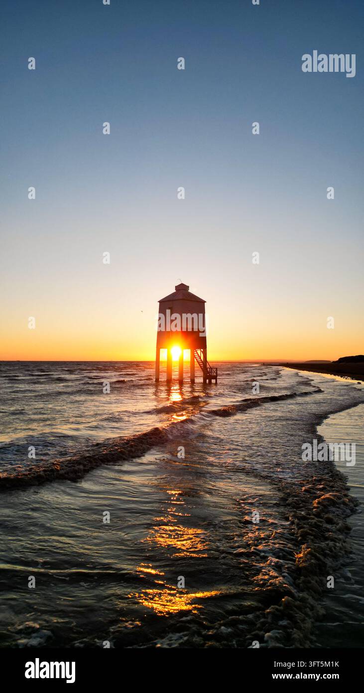 Vista aerea del faro storico di Burnham-on-Sea Low che si erge nella marea al tramonto con luce dorata che si riflette sulla sabbia bagnata e sul mare, Burnham Foto Stock