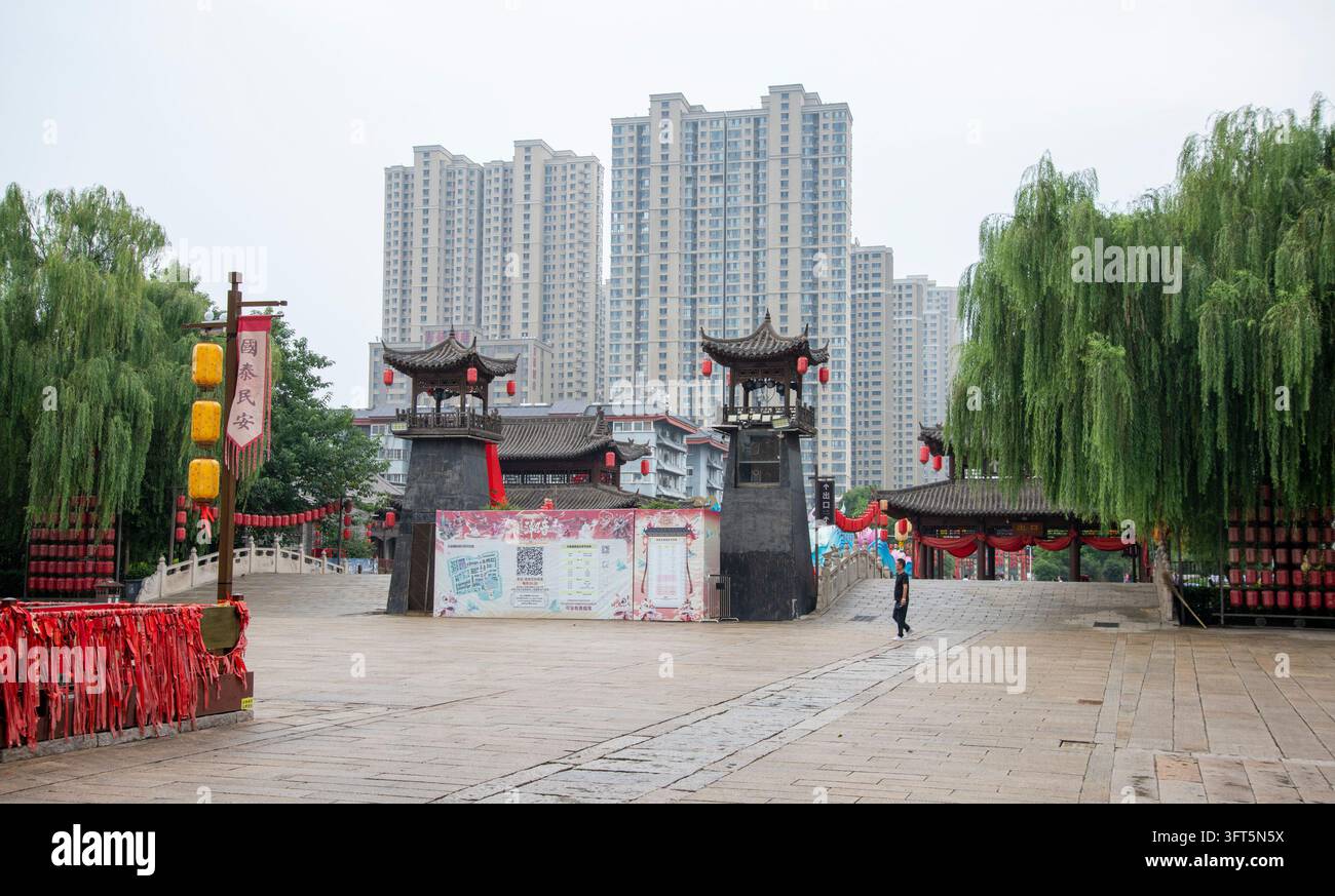Torri-porta in stile tradizionale e salici su una piazza lastricata, con blocchi di appartamenti sullo sfondo a Luoyang, Henan, Cina. Foto Stock