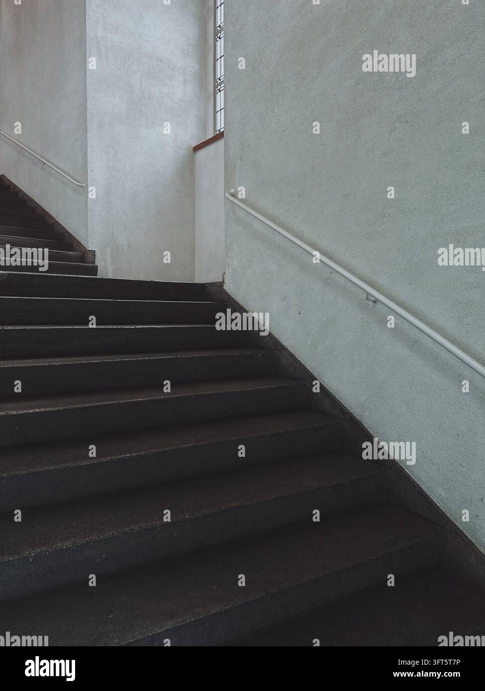 Scatto architettonico semplice e sobrio di scale scure e pareti in cemento strutturato all'interno di un edificio storico. Foto Stock