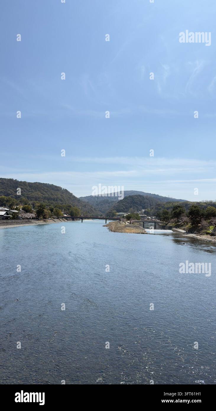 Ampio fiume calmo che scorre tra colline boschive sotto un cielo blu - Immagine stock catturata con smartphone