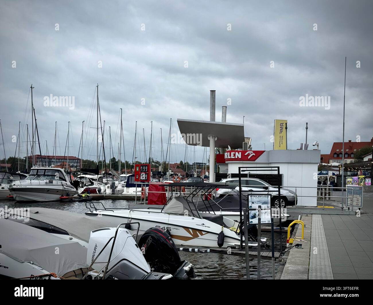 Una fotografia orizzontale che cattura una stazione di servizio marina Orlen in un porto affollato, con barche a motore ormeggiate, yacht e un cartello dei prezzi del carburante - Immagine stock catturata con smartphone