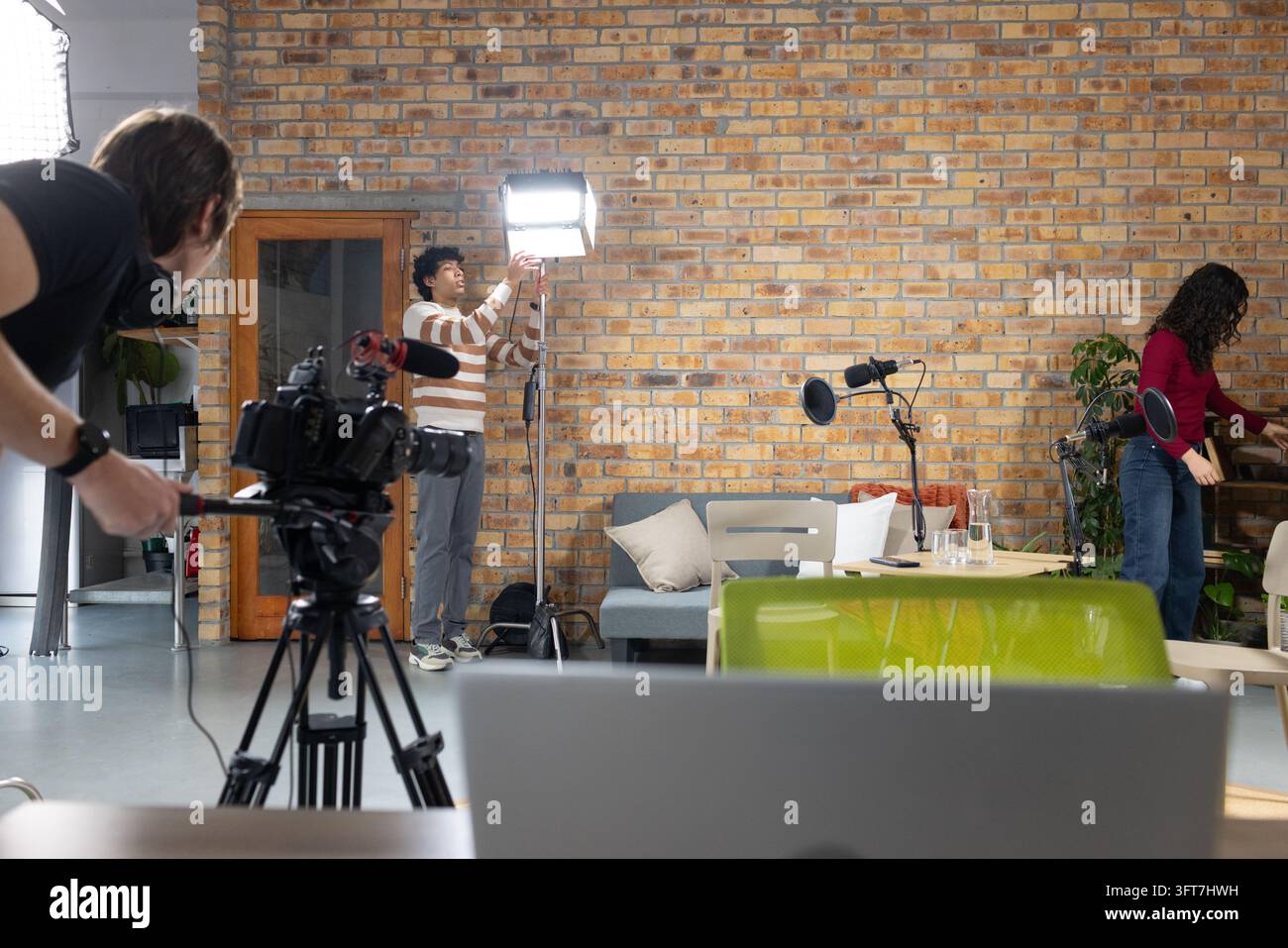 Equipaggio diversificato che regola il pannello LED, gestisce la telecamera su treppiede, sistema il laptop e gli oggetti di scena nel salone Foto Stock