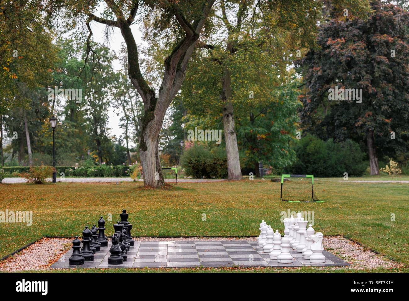 Vista di un grande set di scacchi da giardino con grandi pezzi bianchi e neri in plastica disposti su una scacchiera a scacchi in un tranquillo parco pubblico con erba verde e g Foto Stock