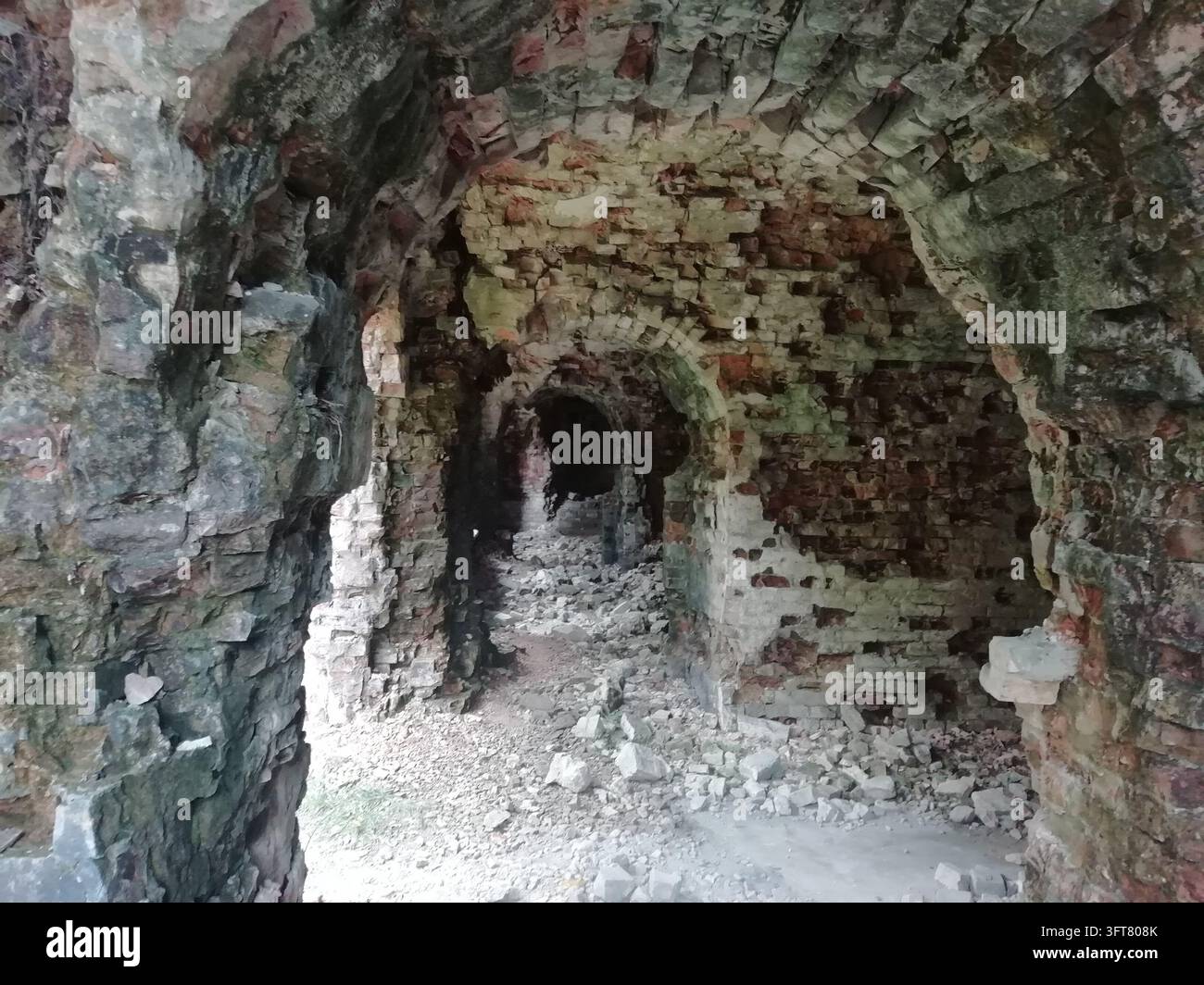 Antico arco in muratura rovinato che si apre su un interno di pietra e mattoni sgretolati Foto Stock