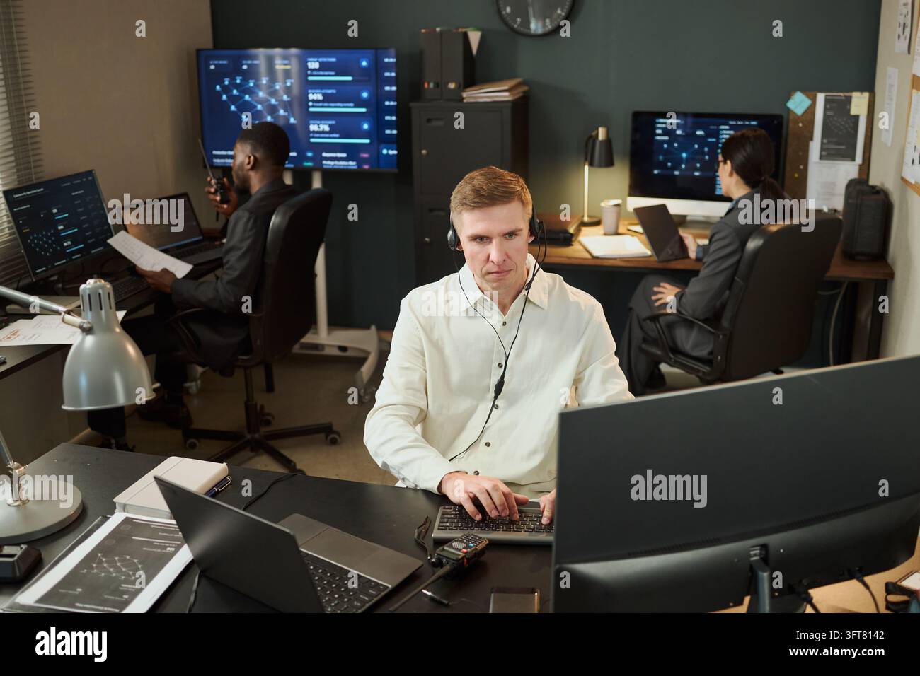 Uomo con auricolari che lavora al computer in un ufficio di sicurezza informatica Foto Stock