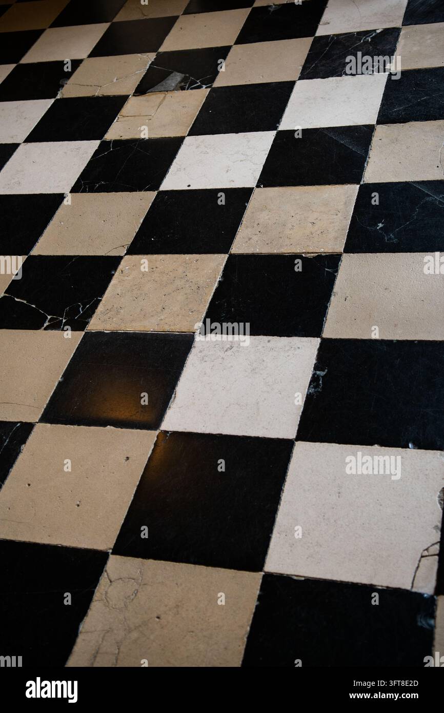 Un pavimento in marmo a scacchi neri e crema forma un motivo geometrico di piastrelle quadrate consumate in un interno parigino. Foto Stock