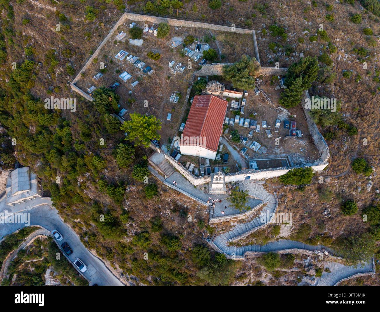 Vista aerea del monastero storico di Santa Maria a Dhermi, che mostra una chiesa con tetto di tegole rosse circondata da un cimitero con mura di pietra e sentieri di pietra tortuosi Foto Stock