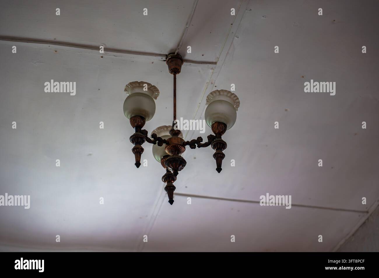 Lampadario a tre bracci montato su soffitto bianco. Presenta sfere in vetro satinato con collari decorativi e ornamenti in bronzo scuro. Foto Stock