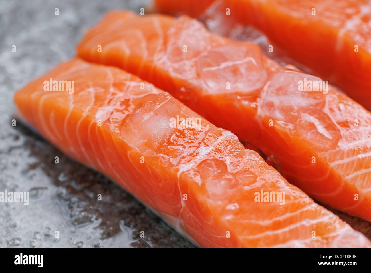 Filetti di salmone crudo con ghiaccio che si scioglie, evidenziando una nutrizione sana, un alto contenuto di proteine, acidi grassi omega e una qualità premium dei frutti di mare Foto Stock