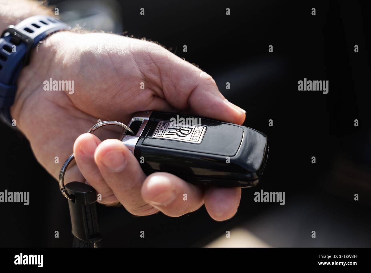 Ljubljana, Slovenia - 14 settembre 2026: Una mano tiene un portachiavi Rolls Royce vicino a un veicolo di lusso all'aperto. Foto Stock