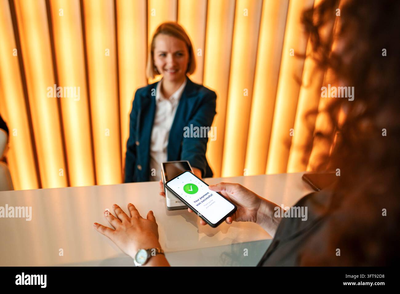 Donna che paga senza contatto con lo smartphone alla reception dell'hotel Foto Stock