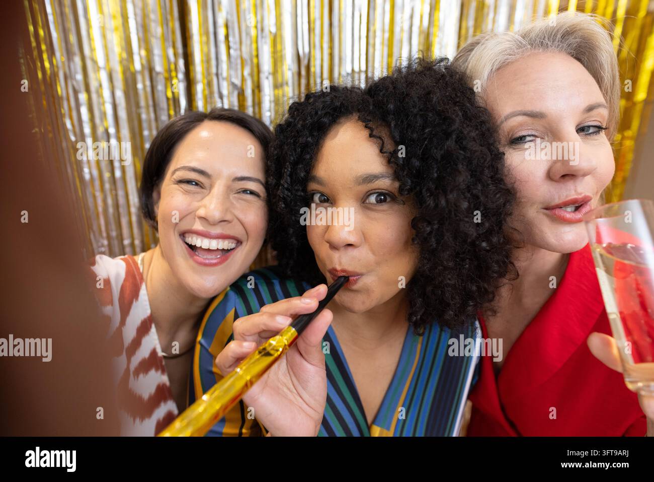Diverse amiche che posano e ridono a un banchetto di festa con corno dorato, flûte di champagne, frange Foto Stock