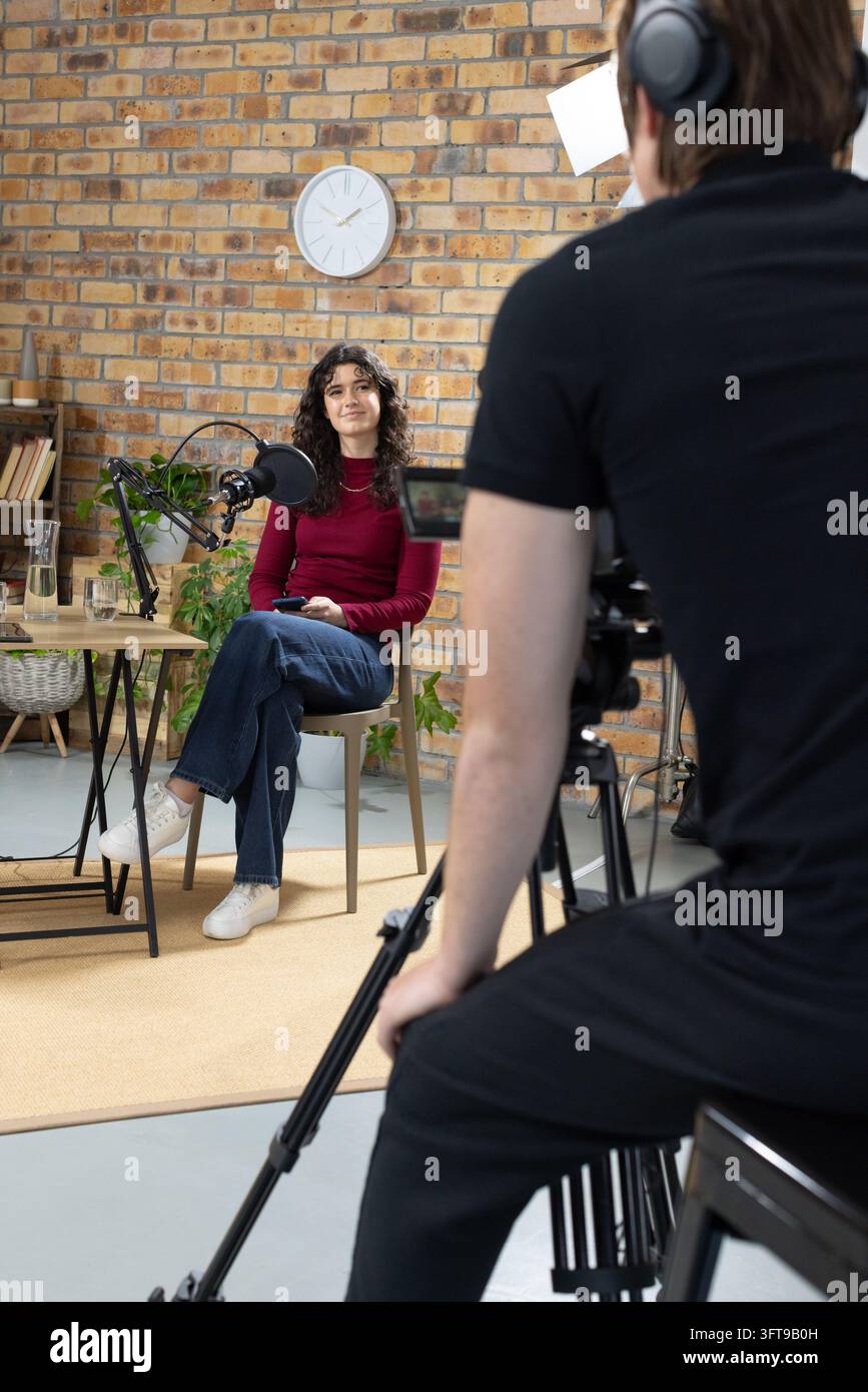 Ospite donna seduta e operatore uomo che filma la telecamera in studio, ospite rivolta verso il microfono Foto Stock