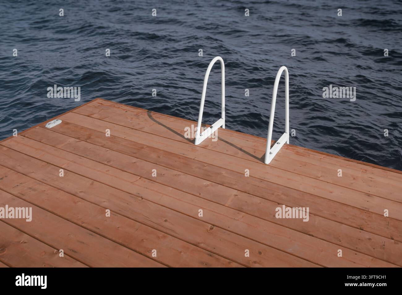 Pontile di legno vuoto con una scala in metallo sopra acqua scura e increspata. Foto Stock