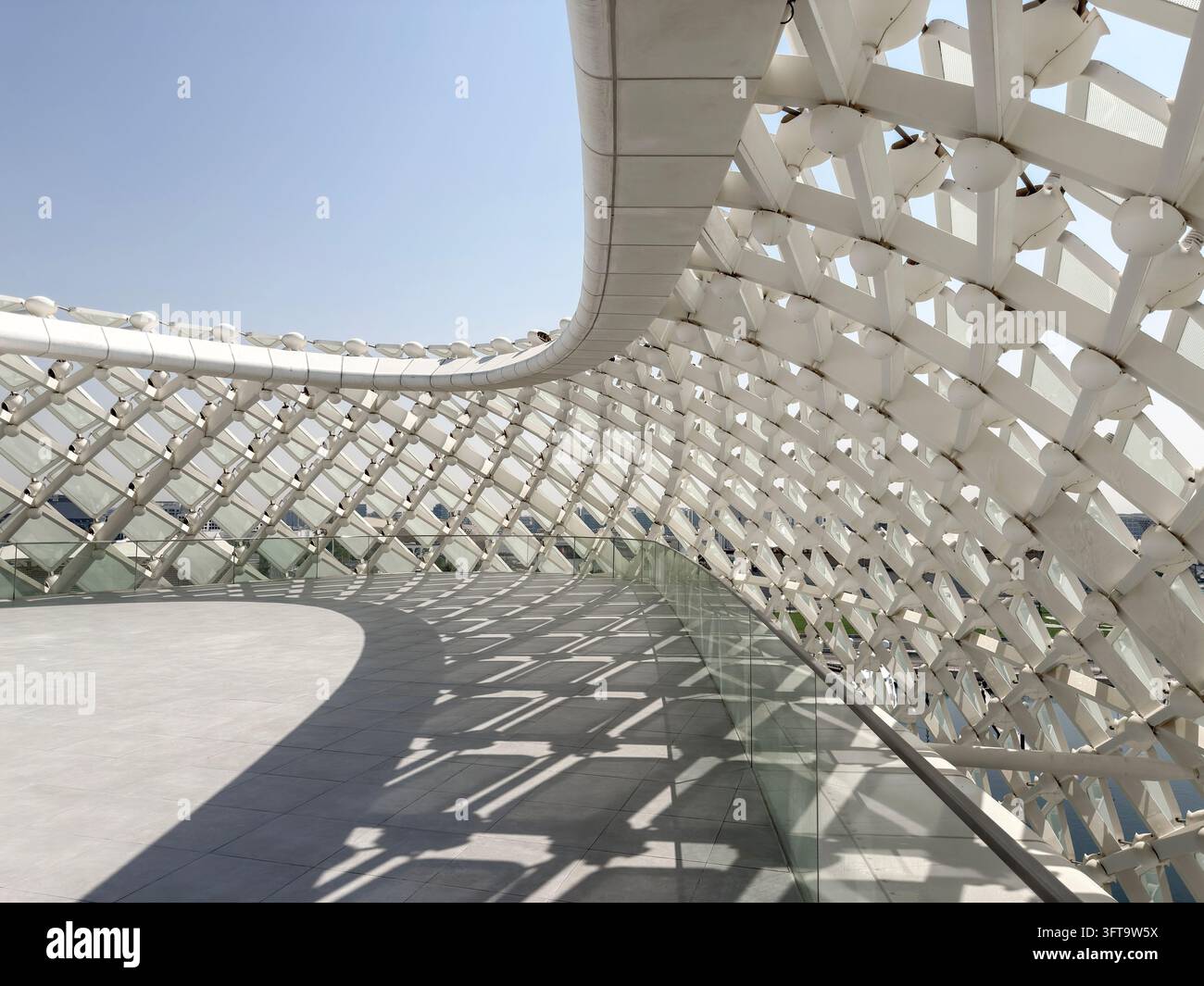 Passaggio pedonale futuristico con tettoia geometrica bianca, ringhiera in vetro e ombre drammatiche della luce del sole, architettura contemporanea con linee curve Foto Stock