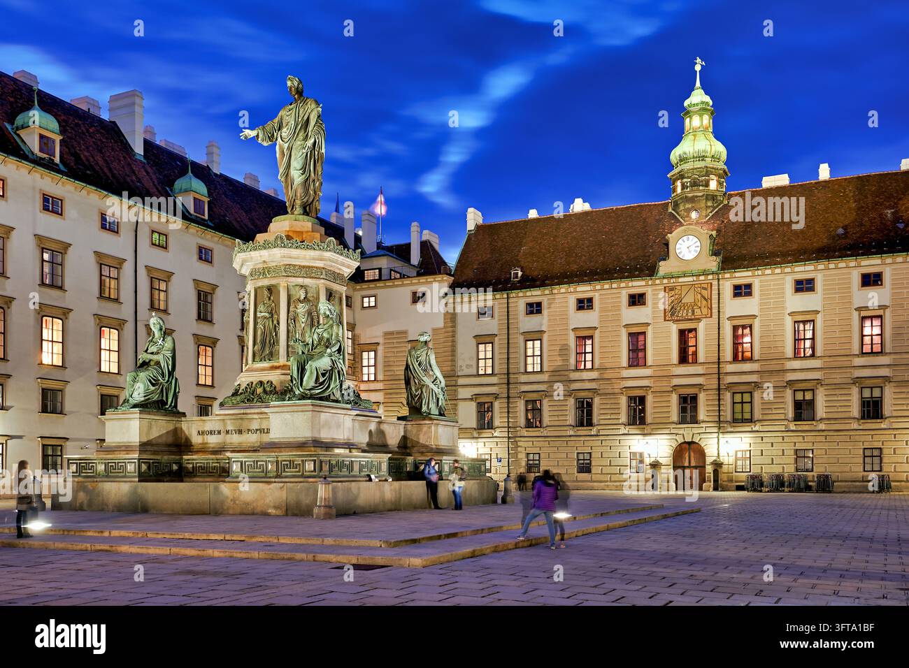 Statua di bronzo di Kaiser Franz I nel cortile In der Burg davanti all'ala Amalienburg, Austria, illuminata all'ora blu con turisti che passano. Foto Stock