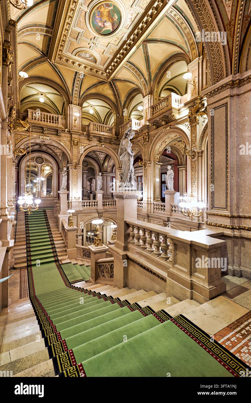 Gradini di marmo con tappeto verde conducono oltre statue allegoriche, archi dorati e soffitti dipinti all'interno della Wiener Staatsoper in stile neorenaissance. Foto Stock