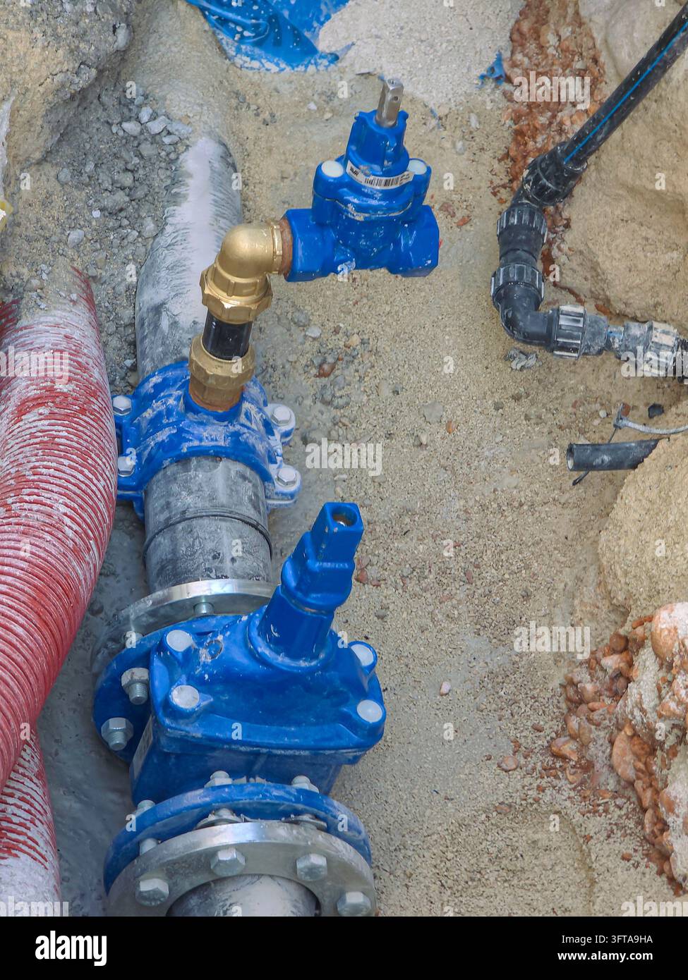 Vista ad angolo alto di un'installazione sotterranea di tubazioni per l'approvvigionamento idrico municipale in una trincea scavata, con valvole a saracinesca in ghisa blu, pesante Foto Stock