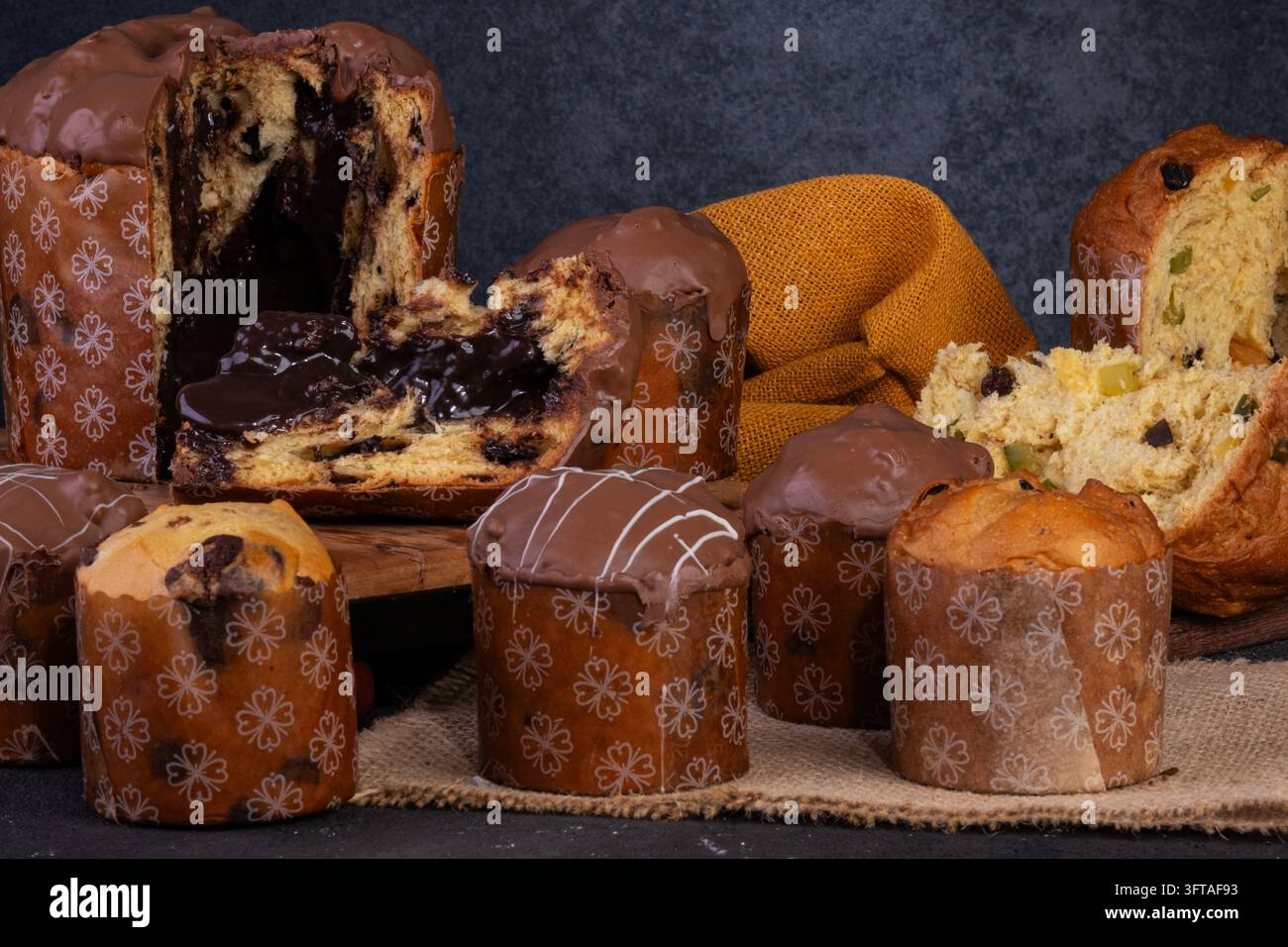 Una esibizione appetitosa di vari panettone su uno sfondo scuro. A sinistra, un grande panettone ricoperto di cioccolato è tagliato per rivelare un Foto Stock