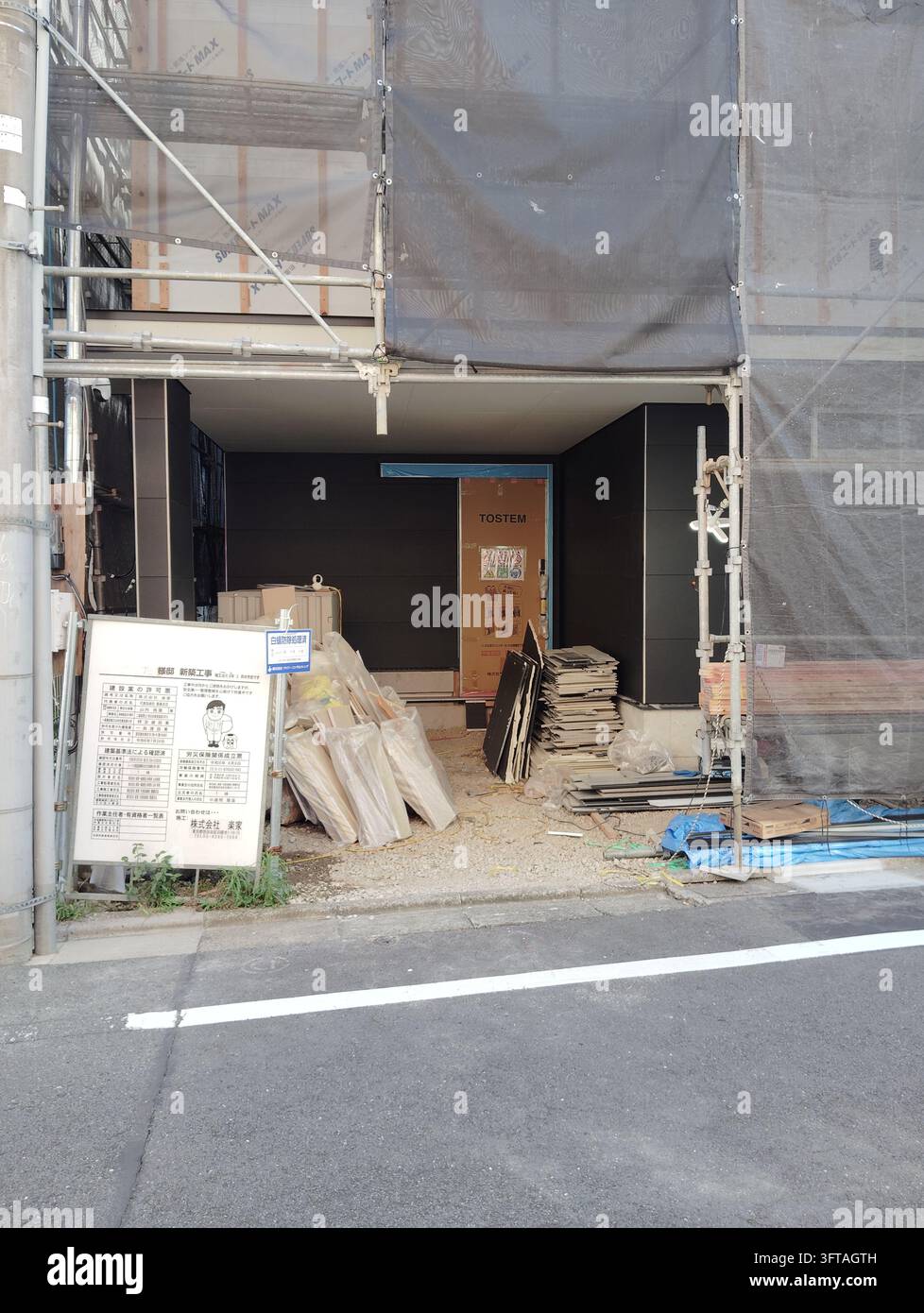 Cantiere edile con impalcatura, rete protettiva e materiali da costruzione impilati lungo una strada stretta a Tokyo, Giappone. Foto Stock
