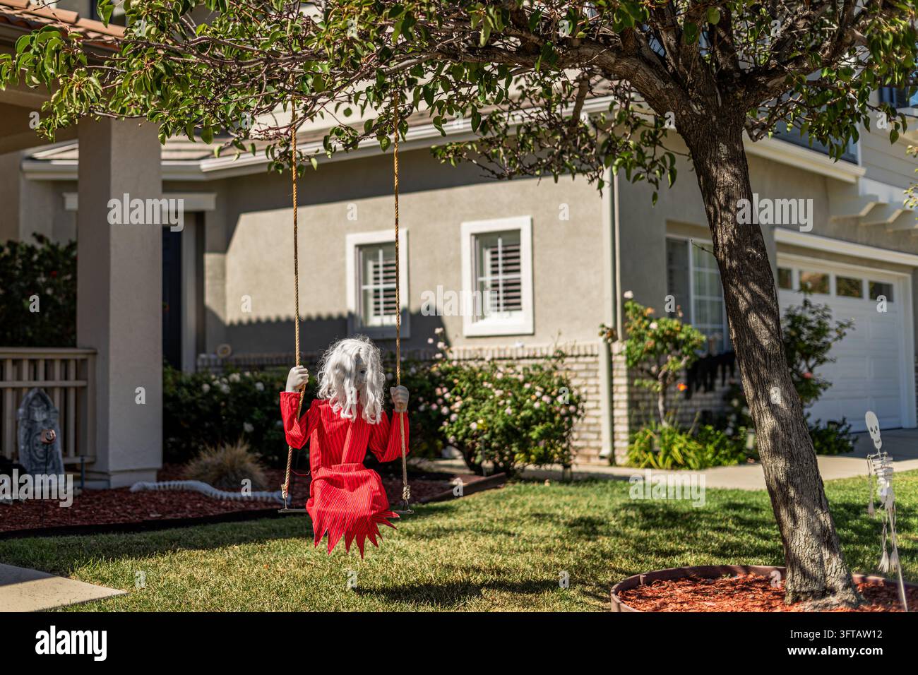 Los Angeles, California, USA - 14 ottobre 2026: Decorazione di Halloween con figura spettrale in costume a righe rosse seduta su un’altalena da giardino sotto t Foto Stock
