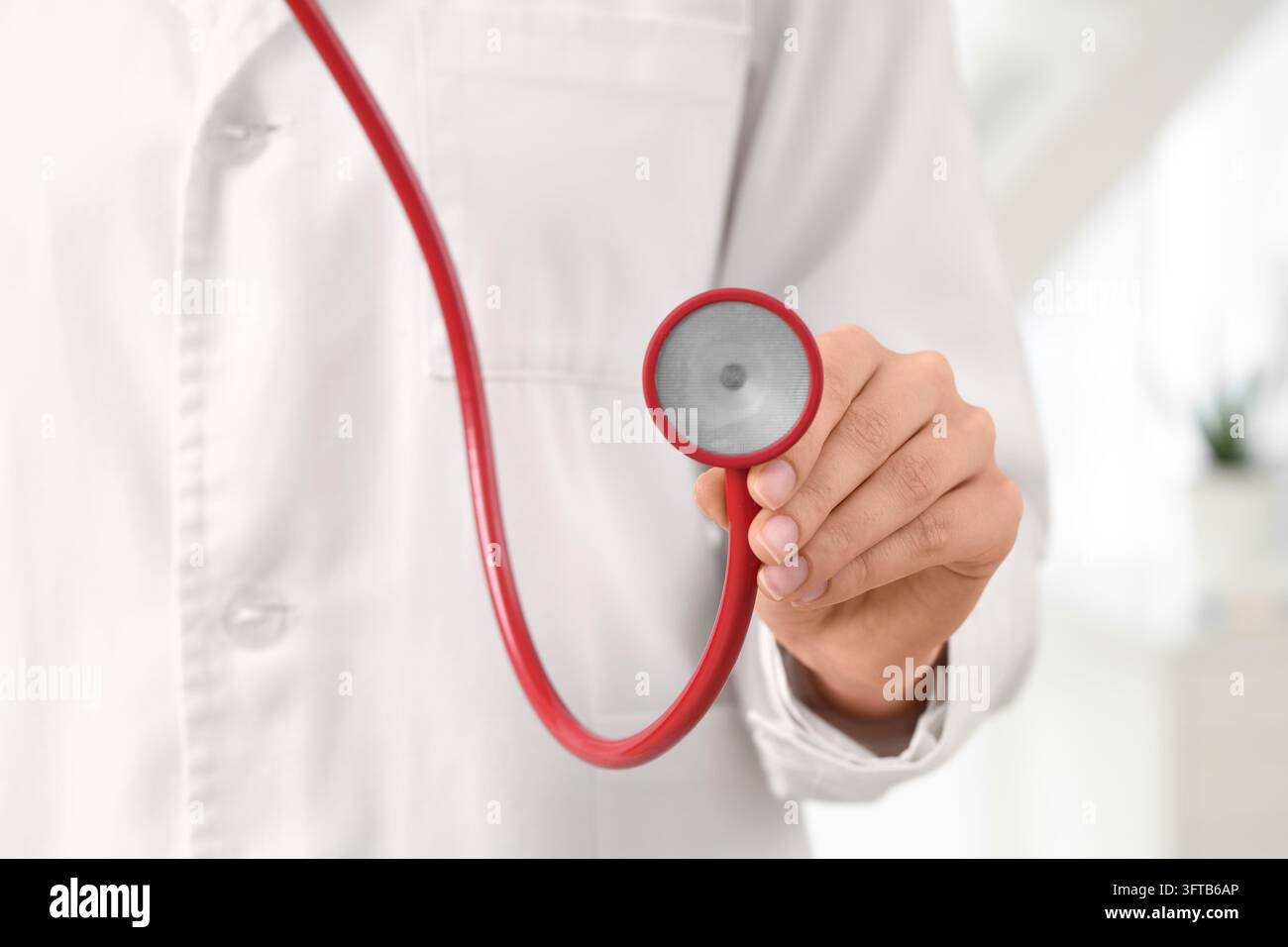 Diagnostica sanitaria ed esame medico, medico che tiene uno stetoscopio rosso per il controllo del paziente in un ambiente clinico con cure professionali Foto Stock