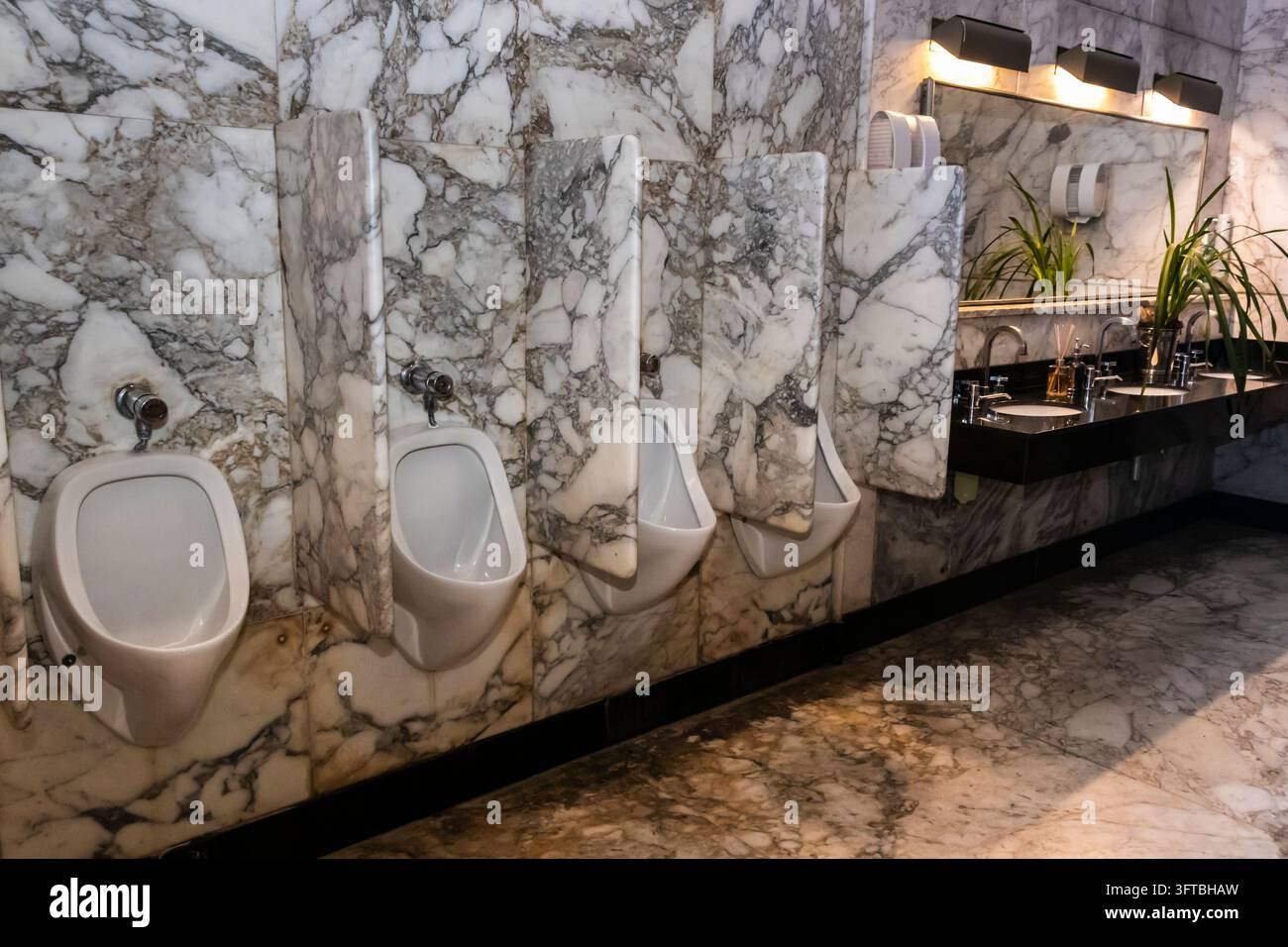 Filera di urinali moderni in ceramica bianca separati da pannelli divisori in marmo pesante di lusso in un bagno pubblico commerciale di fascia alta. L'architettura interna Foto Stock
