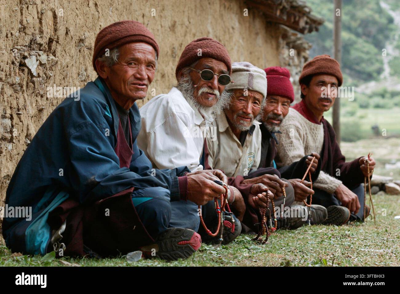 Un gruppo di anziani fuori dal complesso murato del monastero di Rachen nella remota regione di Tsum, Nepal. Gli uomini tengono rosari per le preghiere. Foto Stock