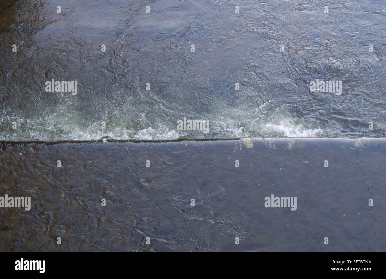 Vista aerea dell'acqua del fiume che scorre sopra una bassa diga con increspature, correnti vorticose e schiuma bianca Foto Stock