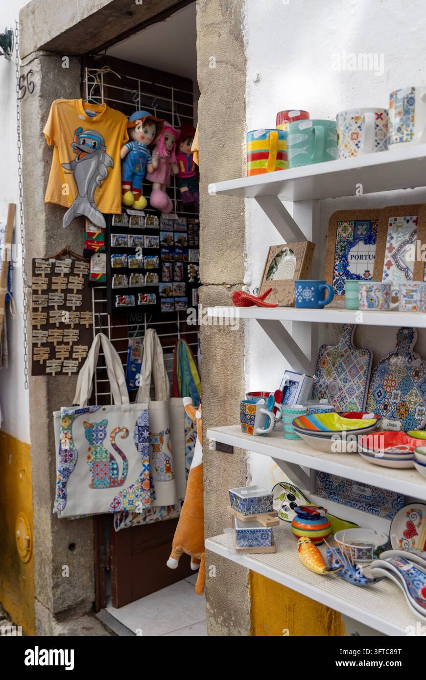 Obidos, Portogallo - 9 maggio 2026: Souvenirs, ceramiche colorate, borse di tela e magliette in esposizione all'aperto in una boutique di regali sulla via principale Rua Direita Foto Stock