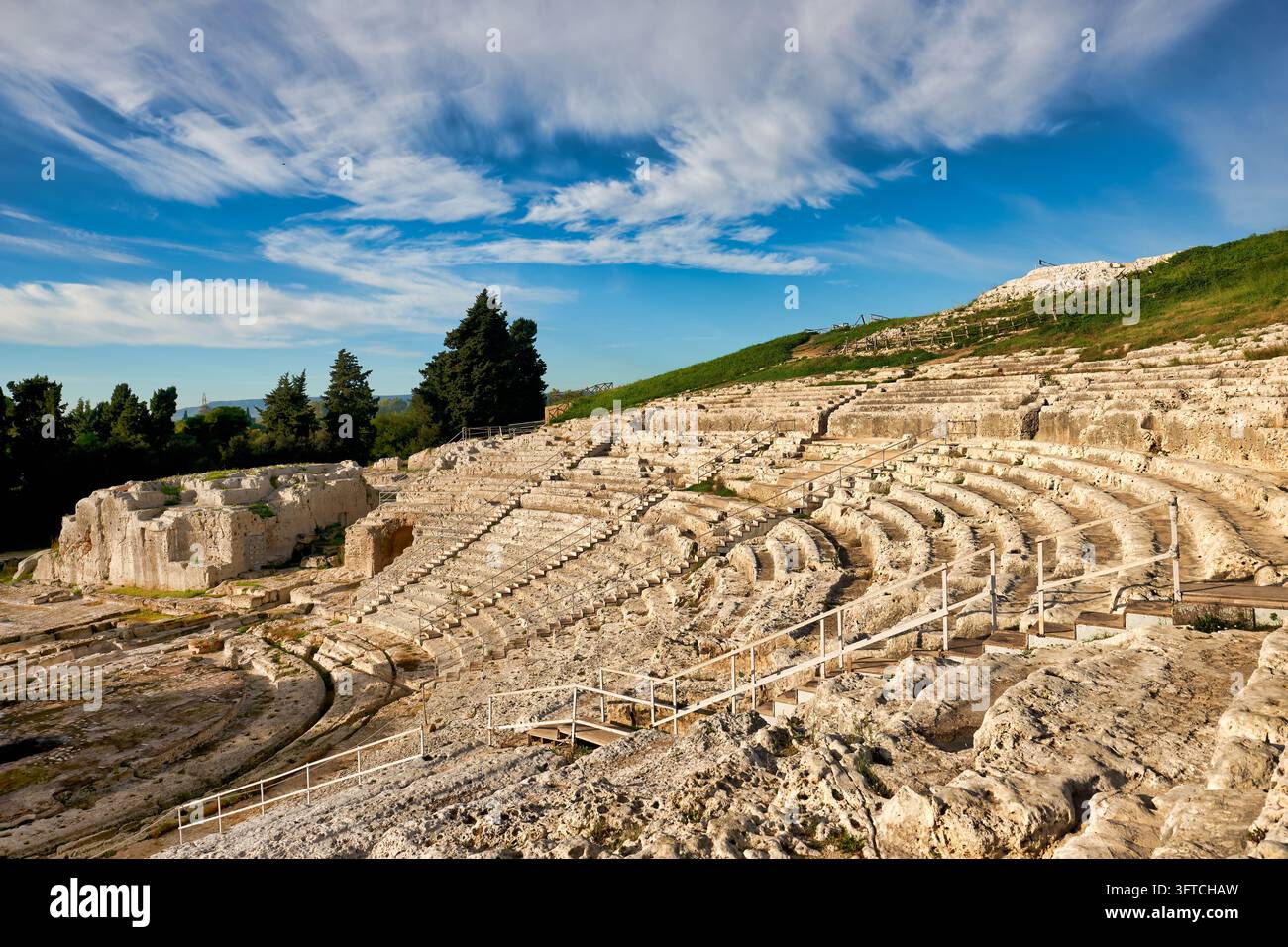 Cavea scavata nella roccia vuota con gradini in calcare nel Parco Archeologico di Neapolis, sito del Patrimonio Mondiale UNESCO, sotto un cielo azzurro con nuvole. Foto Stock
