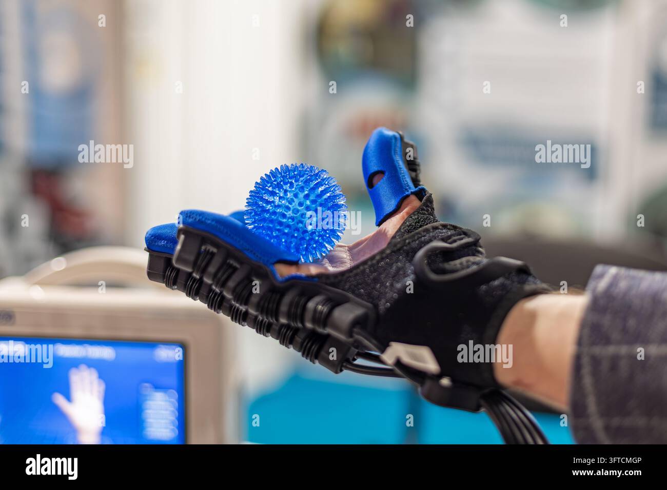 Primo piano di un guanto robotico di riabilitazione che tiene una palla da massaggio blu spinata durante la terapia della mano, dispositivo medico innovativo progettato per assistere le dita Foto Stock