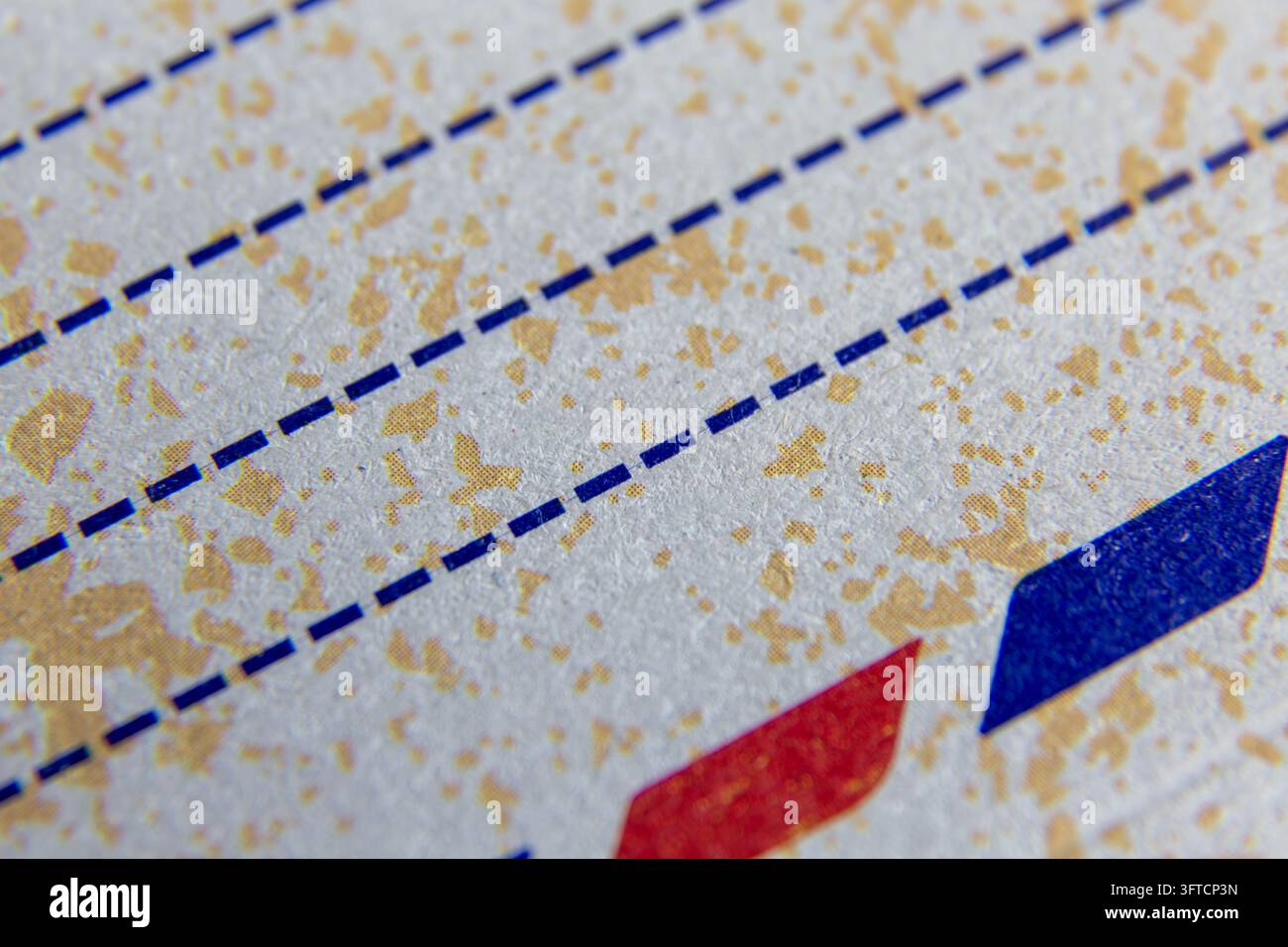 Una fotografia macro in primo piano che mostra linee blu tratteggiate orizzontali stampate su carta avorio ruvida con un motivo dorato screziato. Foto Stock