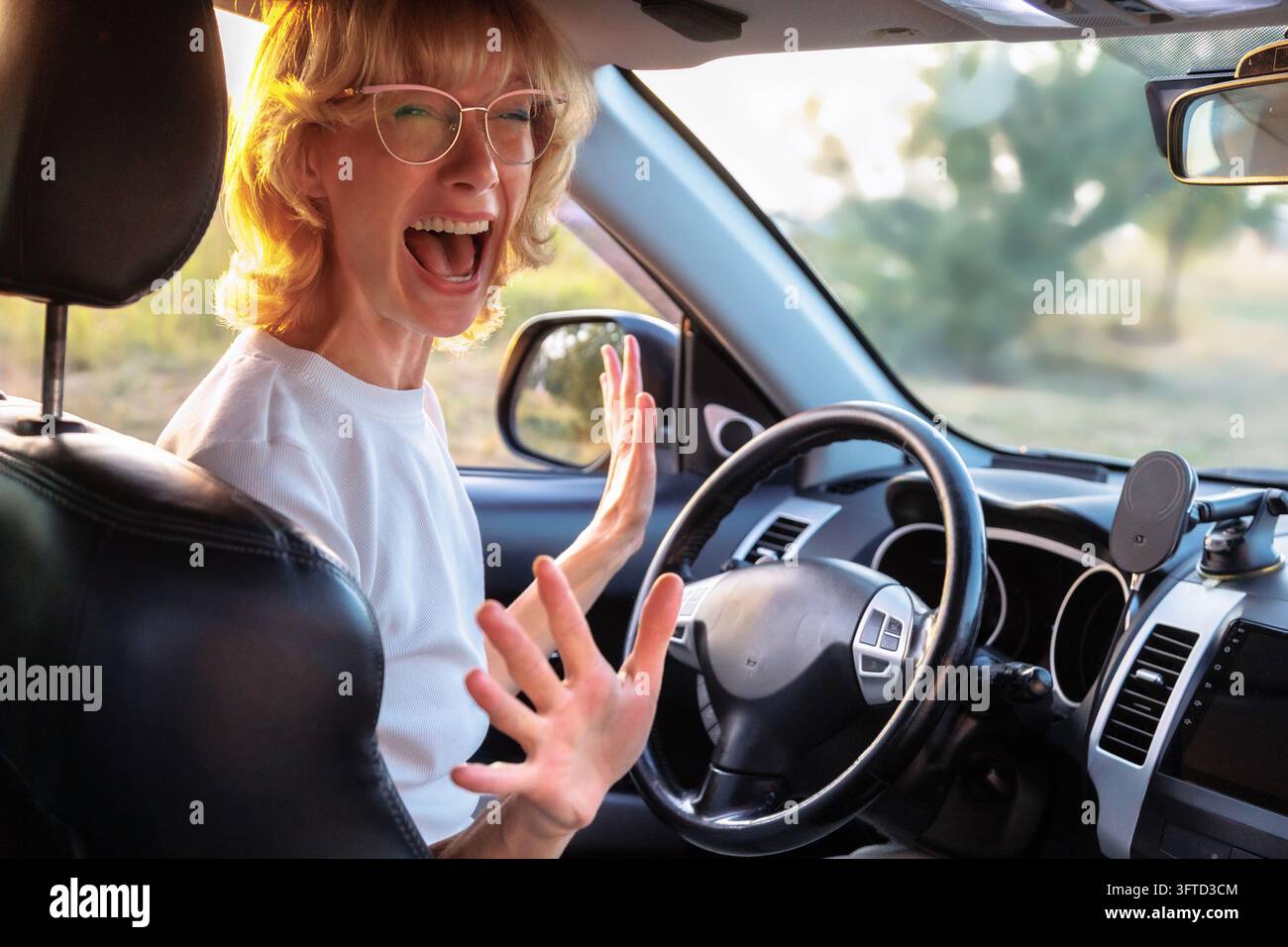 Donna che urla con le mani alzate dietro il volante, esprime panico, frustrazione durante la pratica di guida. Ansia delle principianti, difficoltà di apprendimento Foto Stock