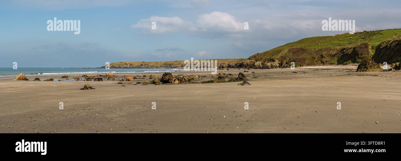 Una vasta spiaggia sabbiosa con rocce sparse e piscine di marea poco profonde sotto un promontorio costiero verde vicino a Porth Colmon sulla costa gallese. Mare calmo, gentile Foto Stock