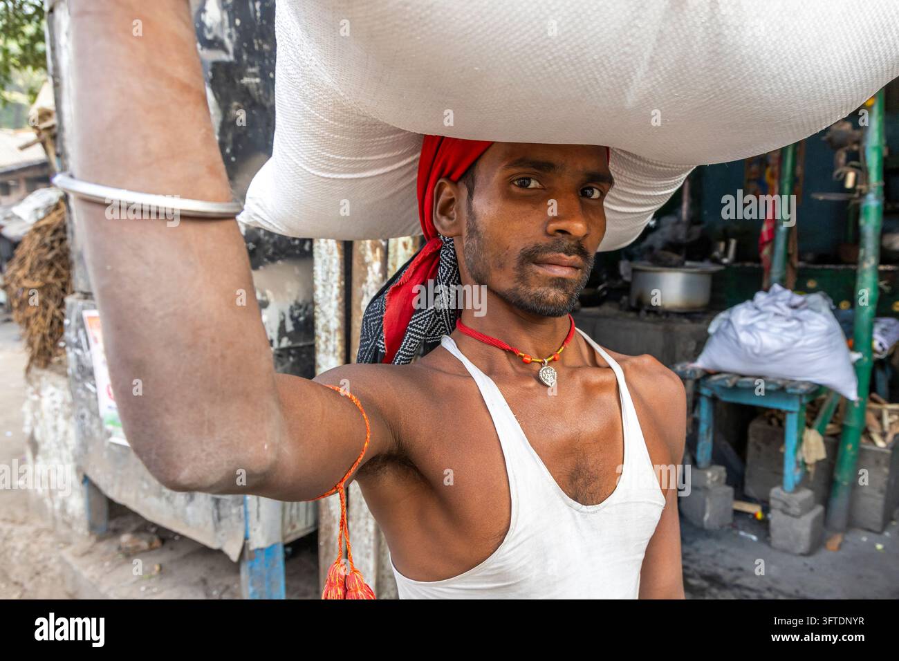 Ritratto ravvicinato di un portatore con un copricapo rosso e un braccialetto d'argento in un gilet bianco accanto alle bancarelle di cibo da strada, Bengala Occidentale, Kolkata, India Foto Stock