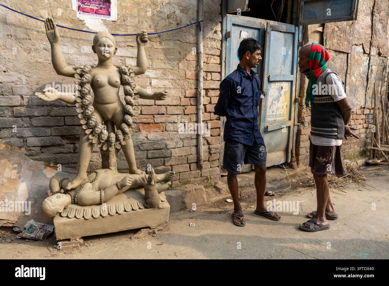 Due operai con sandali chiacchierano in un vicolo con una figura di dea in argilla cruda su una base di loto nel distretto di Kumartuli, Bengala Occidentale, Kolkata, India Foto Stock