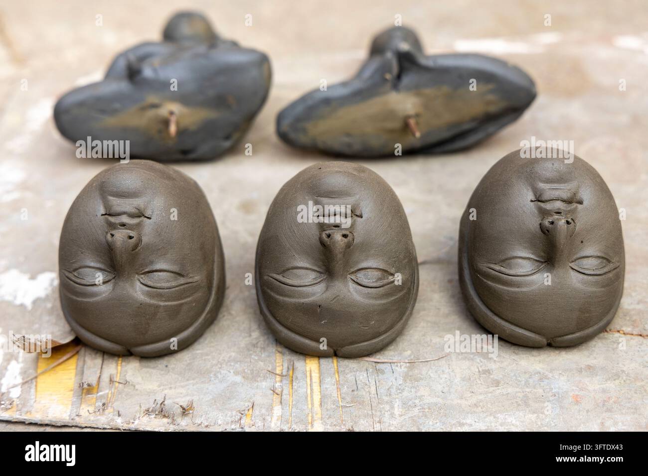 Cinque teste in argilla con gli occhi chiusi posizionate a testa in giù sotto pezzi di argilla curvi scuri su una tavola a Kumartuli, Bengala Occidentale, Kolkata, India Foto Stock