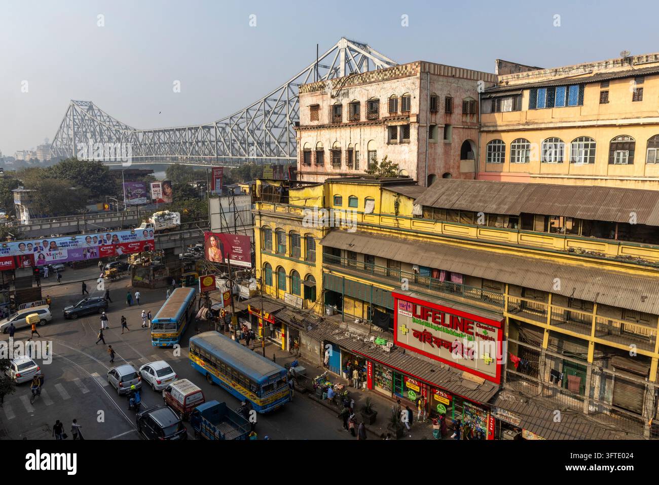 Vista elevata di un incrocio affollato con autobus e auto che passano davanti ad edifici dell'era coloniale e un grande ponte in acciaio, Bengala Occidentale, Kolkata, India Foto Stock
