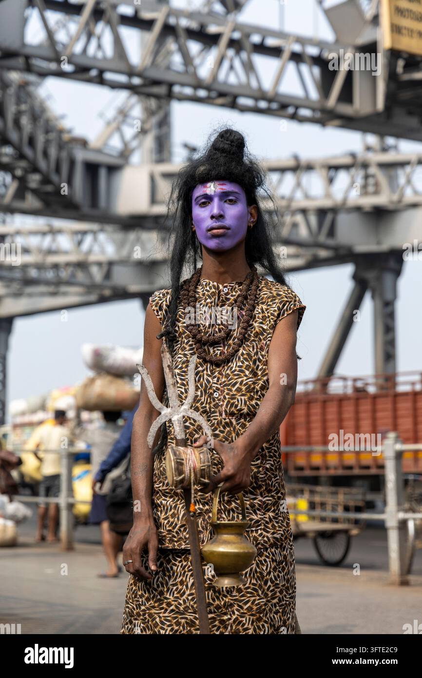 Uomo vestito come il dio indù Shiva con trucco blu sul viso e rosari posa su una strada sotto le travi d'acciaio di un ponte, Bengala Occidentale, Kolkata, India Foto Stock